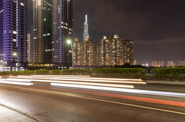 Night time lapse of passing traffic leaving light trails on a busy street with ultra modern high-rise architecture in the background