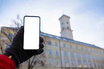 man hand in gloves holding phone with white screen lviv city hall on background