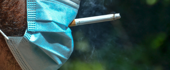 Man trying to smoke a cigarette even though he is wearing a protective coronavirus mask, COVID-19...