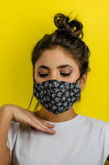 mujer joven de cabello negro usando mascarilla negra con fondo amarillo