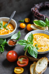 Tomato soup with basil in two ceramic bowls. Lots of tomatoes on the table. Vegetarian food. Red and yellow.