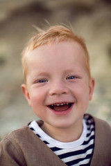 stylish boy child in a vest stands on a pebble beach