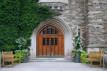 Fototapeta na wymiar double wooden front door with leaded glass and ivy covered stone wall of gothic style college building
