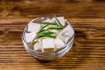 Chopped feta cheese and rosemary in glass bowl on a wooden table