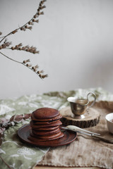 Chocolate pancakes with honey on a brown ceramic plate. Sweet breakfast on a table. Bright interior. Minimalism.