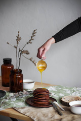 Chocolate pancakes with honey on a brown ceramic plate. Sweet breakfast on a table. Bright interior. Minimalism.