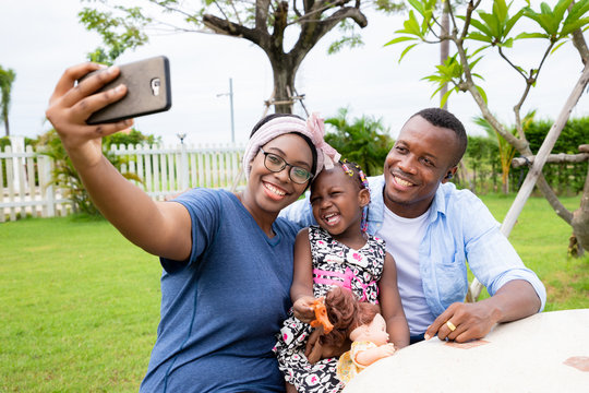 A warm family of black Americans is taking pictures of the family with a smartphone.  They have a bright and friendly smile.  Concepts of relationship building and leisure activities in the garden.