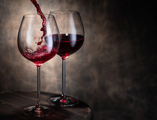Fototapeta na wymiar Trickle of fine red wine pouring from bottle into glass goblets against brown background