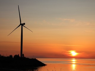 A silhouette of a windmill to produce the windpower on a calm, windless summer evening by the sea.