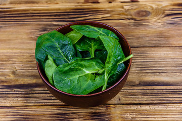Ceramic bowl with spinach leaves on rustic wooden table