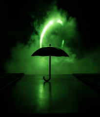 Silhouette of umbrella miniature on table with dark toned foggy background. Creative concept.