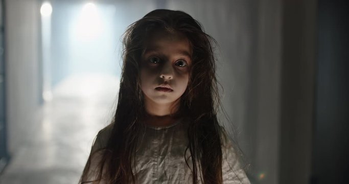 Little creepy girl in ghost costume staring at camera, wearing white sundress. Psycho kid in haunted house - halloween costume party 4k footage