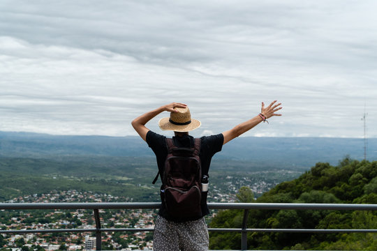 Hombre joven con un brazo abierto y el otro sosteniendo su sombrero mirando la naturaleza