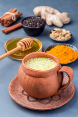 Yellow moon milk with turmeric in clay cup, ingredients on background, vertical