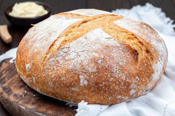 Loaf of Classic Boule bread on dark wooden board with white cloth, horizontal
