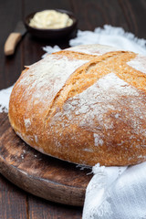 Loaf of Classic Boule bread on dark wooden board with white cloth, vertical