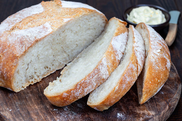 Cutted loaf of Classic Boule bread on dark wooden board with white cloth, horizontal