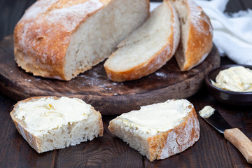 Two piece of fresh backed Classic Boule bread with butter on wooden table, horizontal