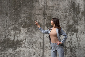 Take a look here! Beautiful young woman pointing away with smile while standing against concrete background
