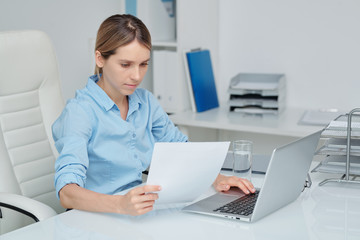 Busy young elegant secretary or accountant reading financial paper by desk