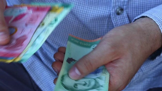 A man in a business shirt counting Costa Rica money, Colones, Various banknotes