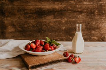 scattered juicy fresh red strawberries on the table with vintage plank. mint leaf. drops and splashes of spilled milk. vegetable cutting board. High quality photo
