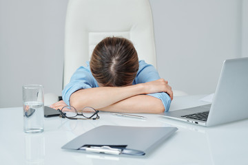 Young exhausted businesswoman keeping her head on crossed arms on desk