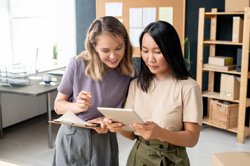 Two happy young businesswomen with digital tablet looking through online orders