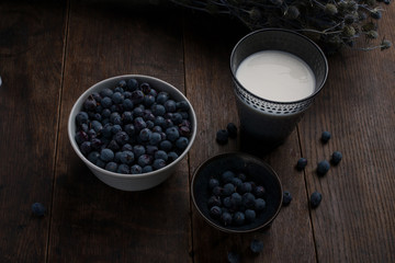 Fototapeta na wymiar Glass of milk, cup and bowl of blueberries and thistle branch on the old wooden table