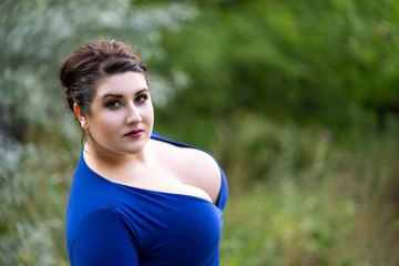 Sexy plus size fashion model in blue dress with a deep neckline outdoors, beautiful fat woman with...