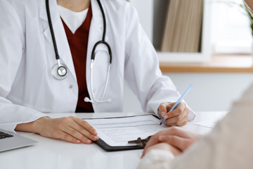 Unknown woman-doctor filling up an application form while consulting patient. Medicine concept