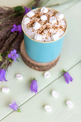 Fototapeta na wymiar Delicious mocha with white marshmallows on an azure background with lilac flowers.