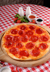 Neapolitan Pepperoni pizza with sausage, salami, cheese, vegetable and tomatoes sauce, served on a wooden board for a dinner in italian restaurant background, top view. Italy food. 