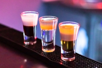 Short drinks at night bar. Three glasses of alcoholic cocktails. Colorful neon light, dark shadows.