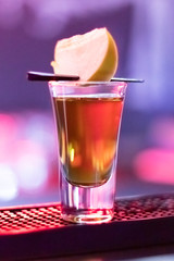 Short drink with a slice of apple at night bar. Fruity alcoholic cocktail. Colorful neon light, dark shadows.