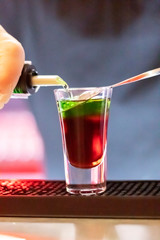 Bartender pours alcohol into a glass. Short drink at night bar. Colorful neon lights, dark shadows.