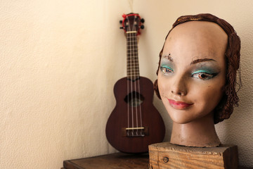 still life of vintage objects like an ukulele and the head of an old mannequin woman with makeup and wig