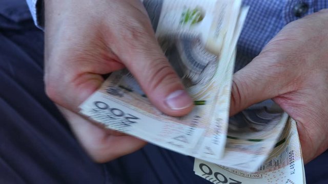 A man in a business shirt is counting Polish money. A large amount of two hundred zloty bills