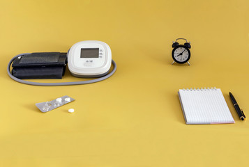 Modern blood pressure monitor, tablets, watch, Notepad, pen on a yellow background. the concept of medicine, blood pressure monitoring