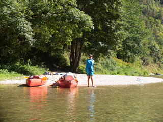 Child wrapped in a towel while standing next to colorful kayaks in riverside