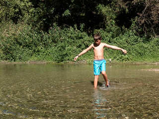 Little boy standing in shallow water in forest in mediterranean country in summer time sunny