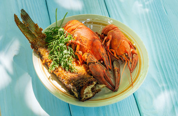 Boiled crayfish and fried fish on plate with a bunch of dill before dinner