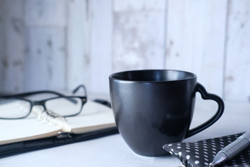 black mug mockup, modern workspace with notepad and eyeglass on table.