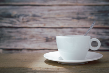 A white hot coffee cup with a spoon in the cup and a saucer is placed on a wooden plate and on a wooden background.front view.