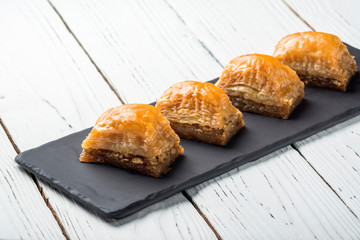 Turkish baklava, oriental sweets on a black dish for serving on a wooden white table. Food photo.