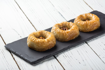 Turkish baklava, oriental sweets on a black dish for serving on a wooden white table. Horizontal format.