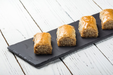 Turkish baklava, oriental sweets on a black dish for serving on a wooden white table. Horizontal format.