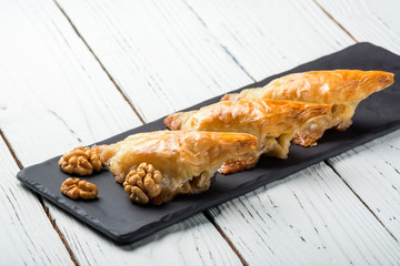 Turkish baklava, oriental sweets on a black dish for serving on a wooden white table. Horizontal format.