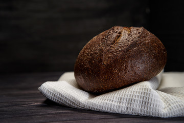 Fresh traditional bread on white kitchen towel. Crisp. Freshly baked brown bread. Rustic style. Horizontal photo close up on black background