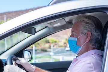 Serious and concentrated senior man wearing surgical mask due to coronavirus  driving the car in sunny day